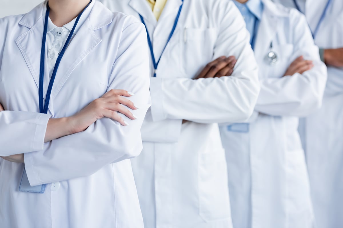 multicultural doctors in white coats standing with crossed arms multicultural doctors in white coats standing with crossed arms