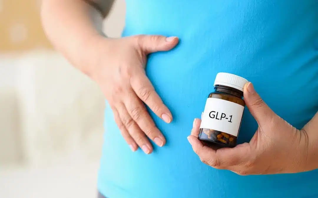 Person in a blue shirt holding a GLP-1 medication bottle against their stomach for weight loss management.
